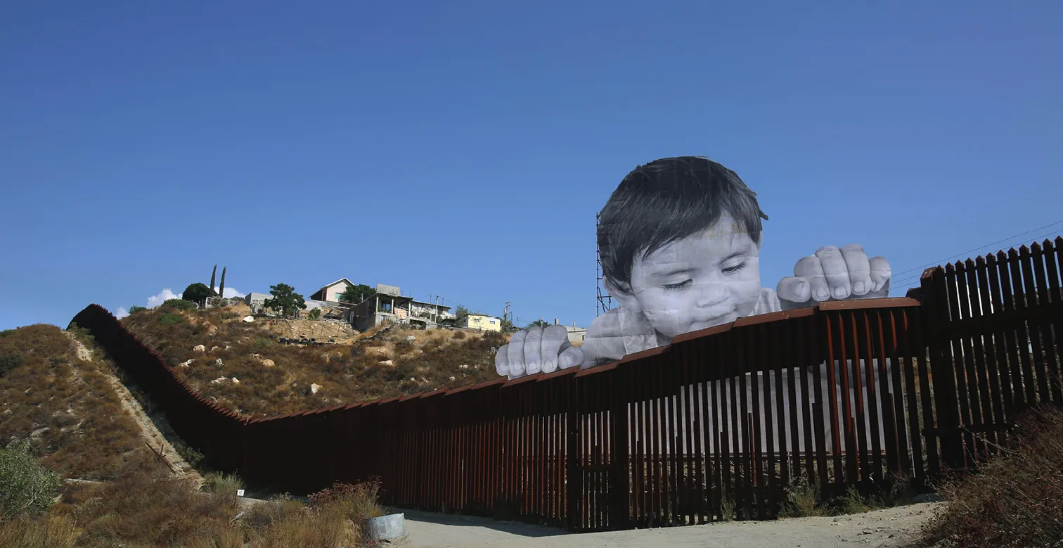 Photographie d'un immense portrait d'enfant surdimensionné, regardant par-dessus un mur frontalier. Comparaison échelle enfant/mur, symbole migration.