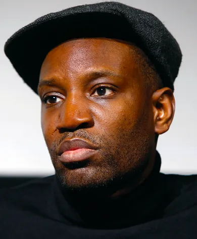 Photographie portrait d'Abd al Malik, rappeur français, vêtu d'un col roulé noir et d'une casquette.