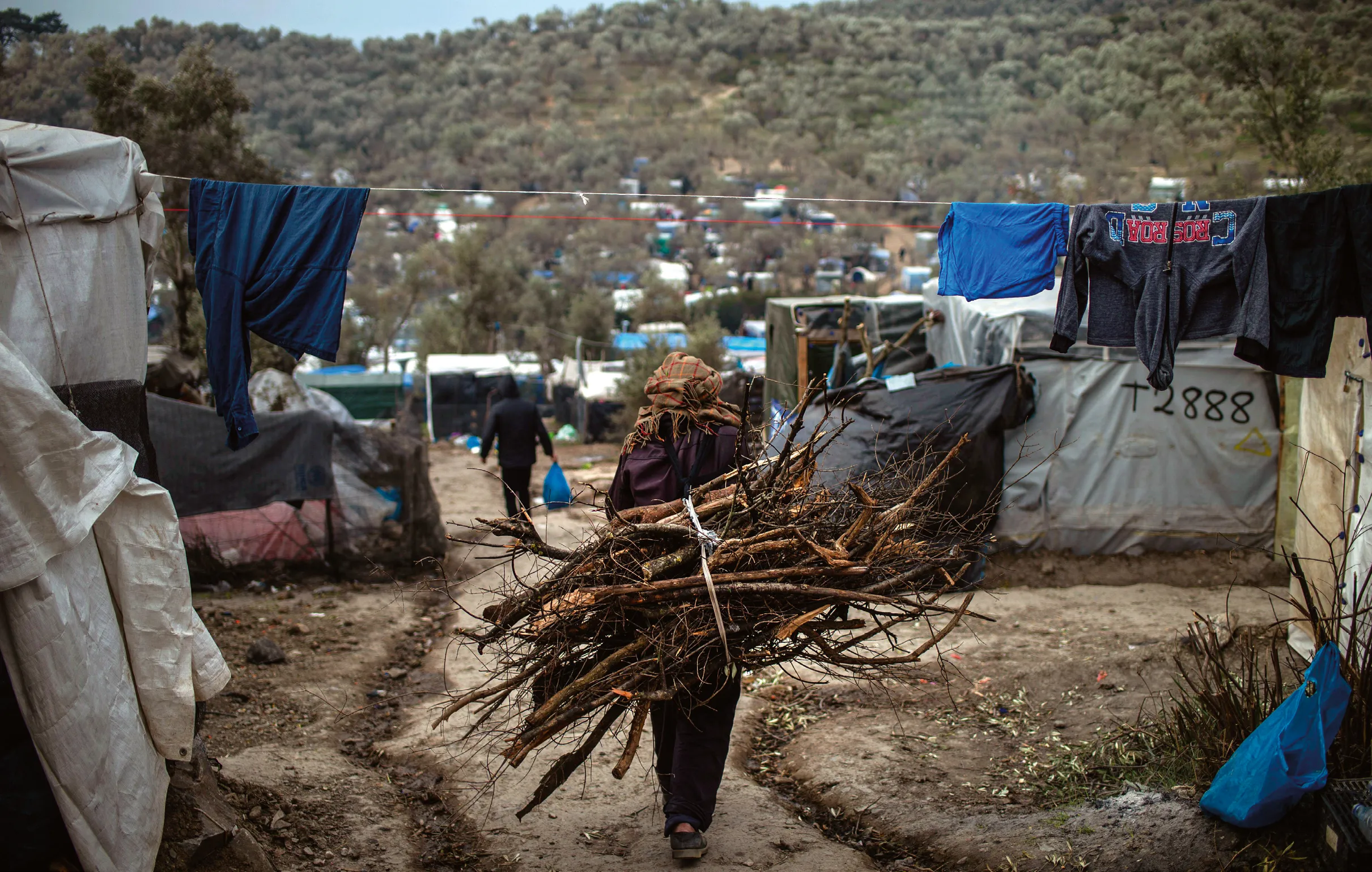 Photographie d'un réfugié portant du bois dans un camp près de Mória, Grèce. Vie quotidienne difficile.